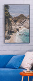 Framed beachscape print on a wall above a blue sofa with a white pillow. Buen Dia art prints San Luis Obispo