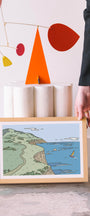 Framed artwork of a coastal scene on a table with abstract art in the background. Buen Dia art prints San Luis Obispo.