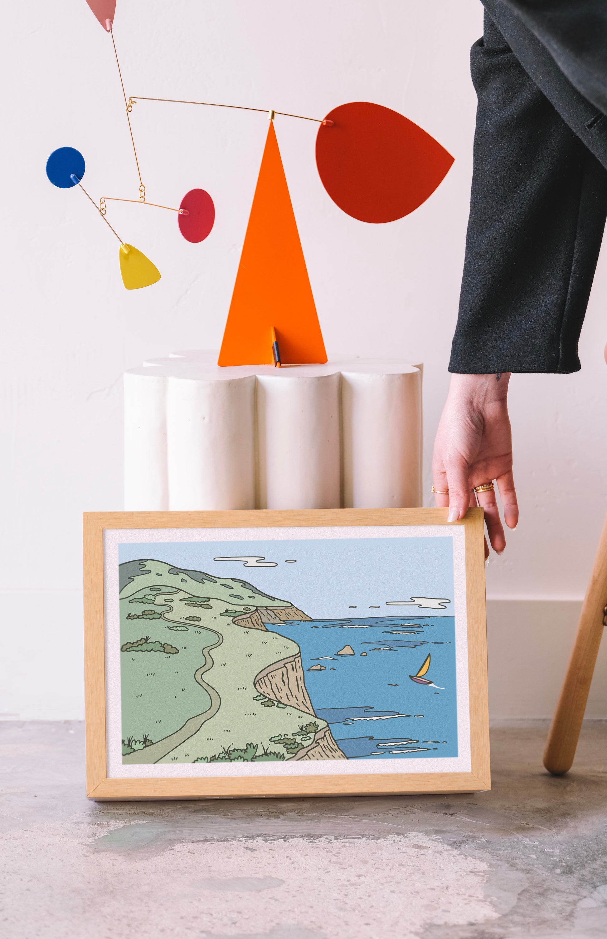 Framed artwork of a coastal scene on a table with abstract art in the background. Buen Dia art prints San Luis Obispo.