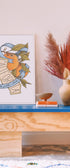 Wooden console table with decorative items including a vase, books, and a framed print on a light-colored wall. Buen Dia art prints San Luis Obispo