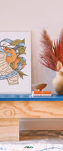 Wooden console table with decorative items including a vase, books, and a framed print on a light-colored wall. Buen Dia art prints San Luis Obispo
