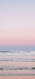 Pastel pink and blue gradient sky over a calm ocean with a sandy beach.