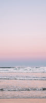 Pastel pink and blue gradient sky over a calm ocean with a sandy beach.