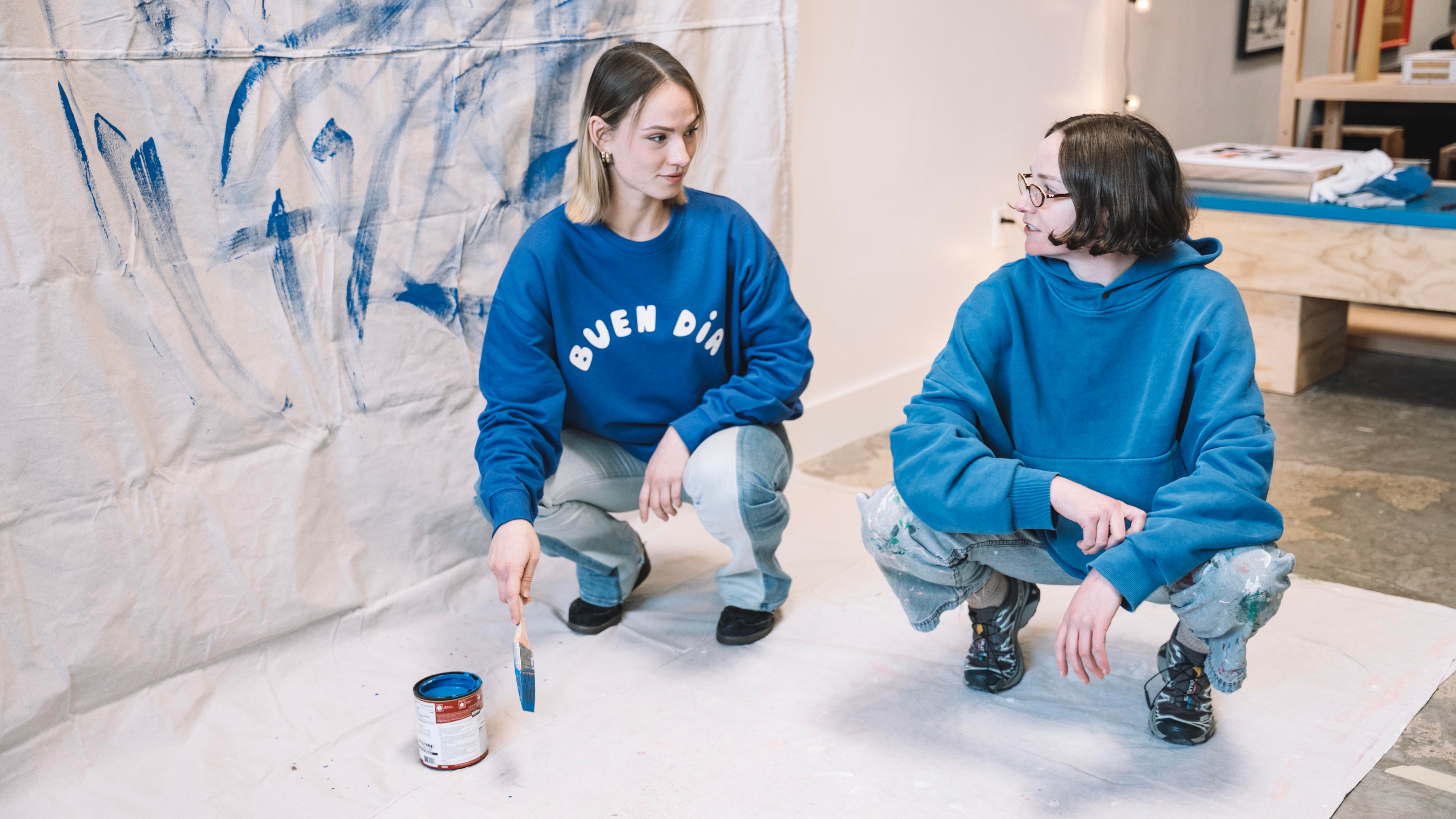 Two people in blue sweatshirts painting a wall with blue paint.