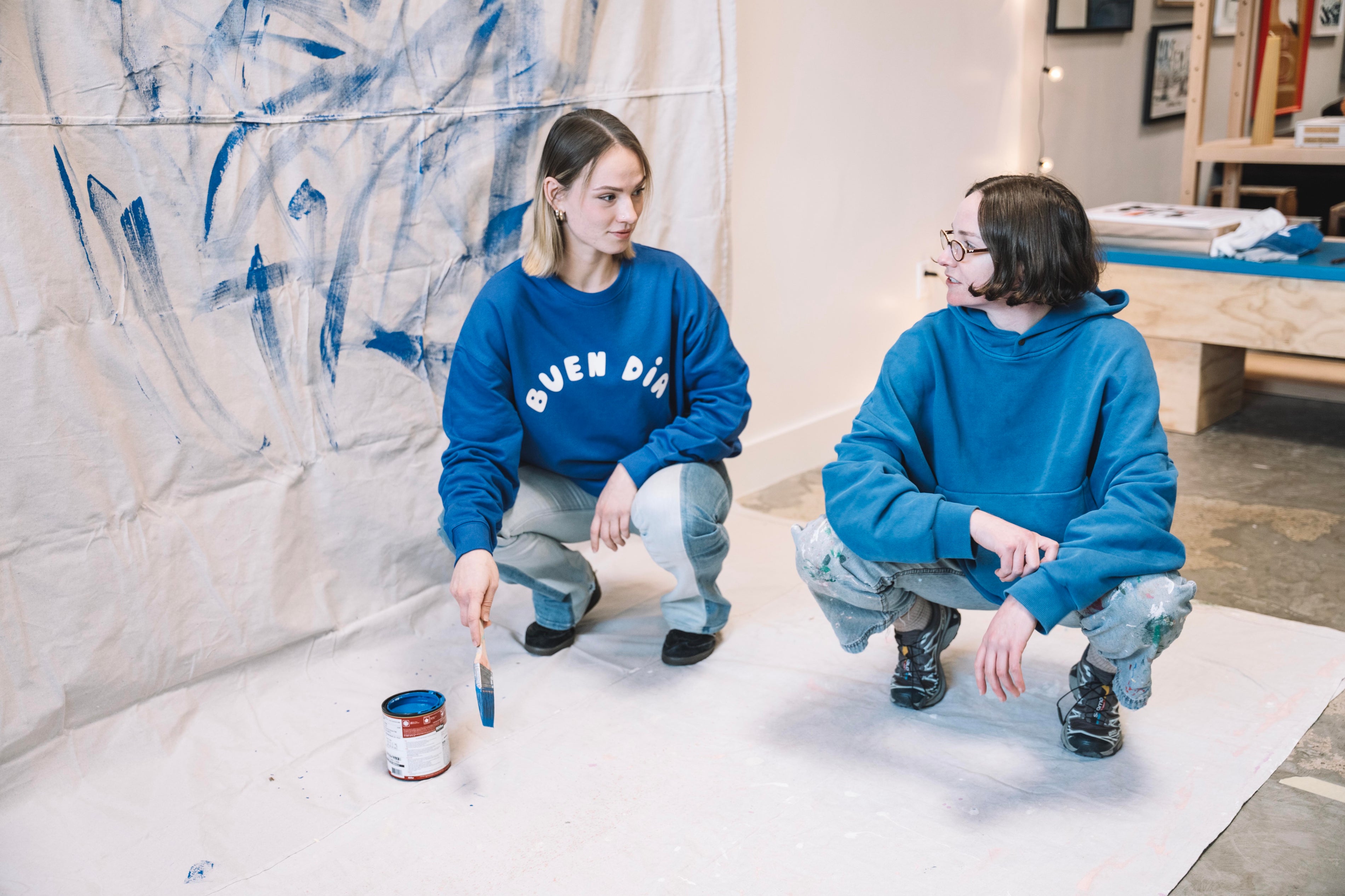 Two people in blue sweatshirts painting a wall with blue paint.