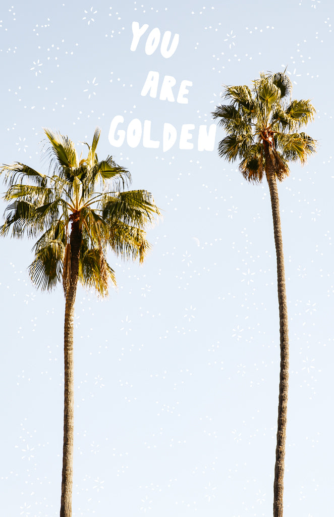 A photographic print featuring two palm trees against a blue sky with the sun setting in the background, and the text 'YOU ARE GOLDEN' overlaid at the top.